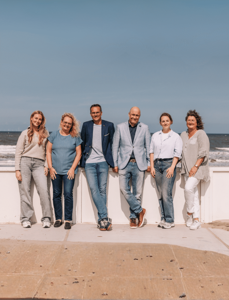 Teamfoto Zandvoort Marketing 2025 met zes teamleden en de zee op de achtergrond